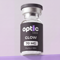 A small glass vial labeled Optic Labs GLOW70 (BPC-157 10mg + GHK-CU 50mg + TB-500 10mg) stands upright against a light purple background. Its black label features white and purple text, similar to other Optic Labs vials. Optic Labs Au